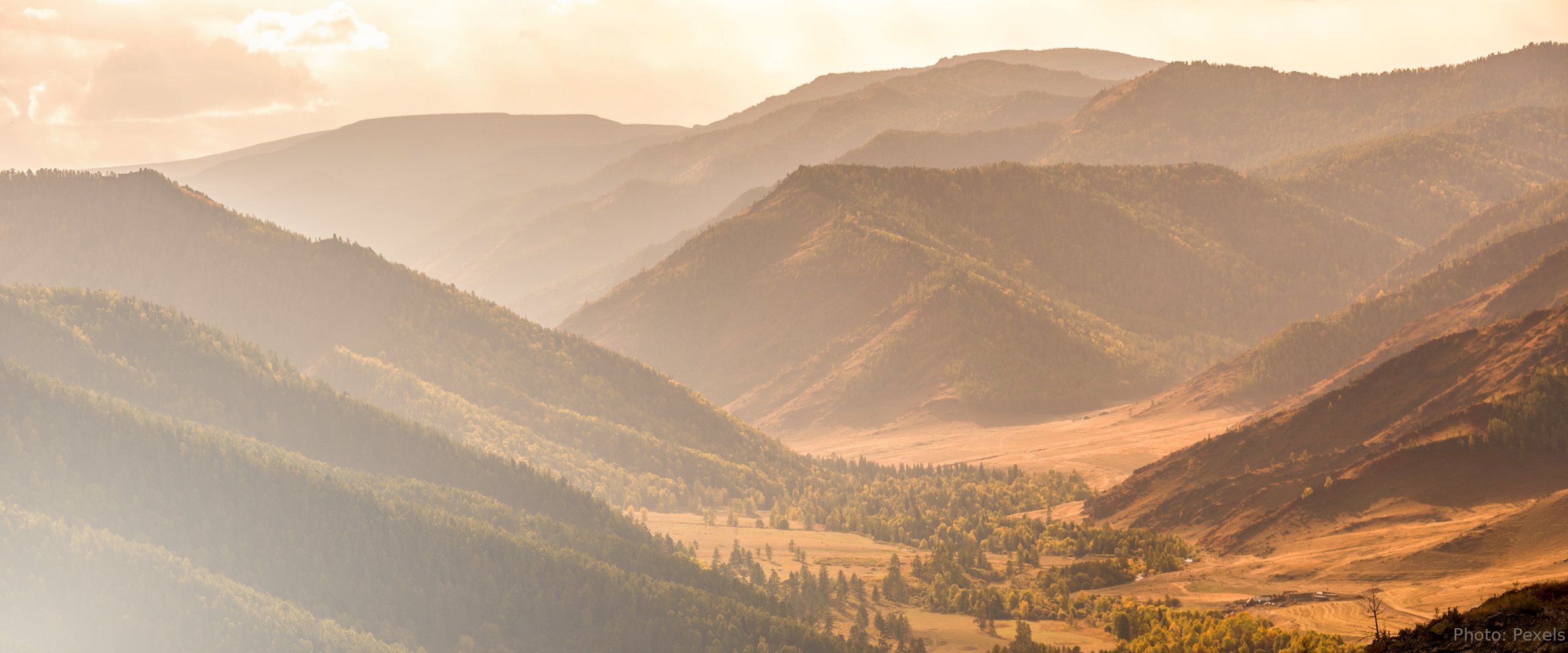 Layered mountain ridges recede into golden evening light, a bright valley floor resting between the high slopes.