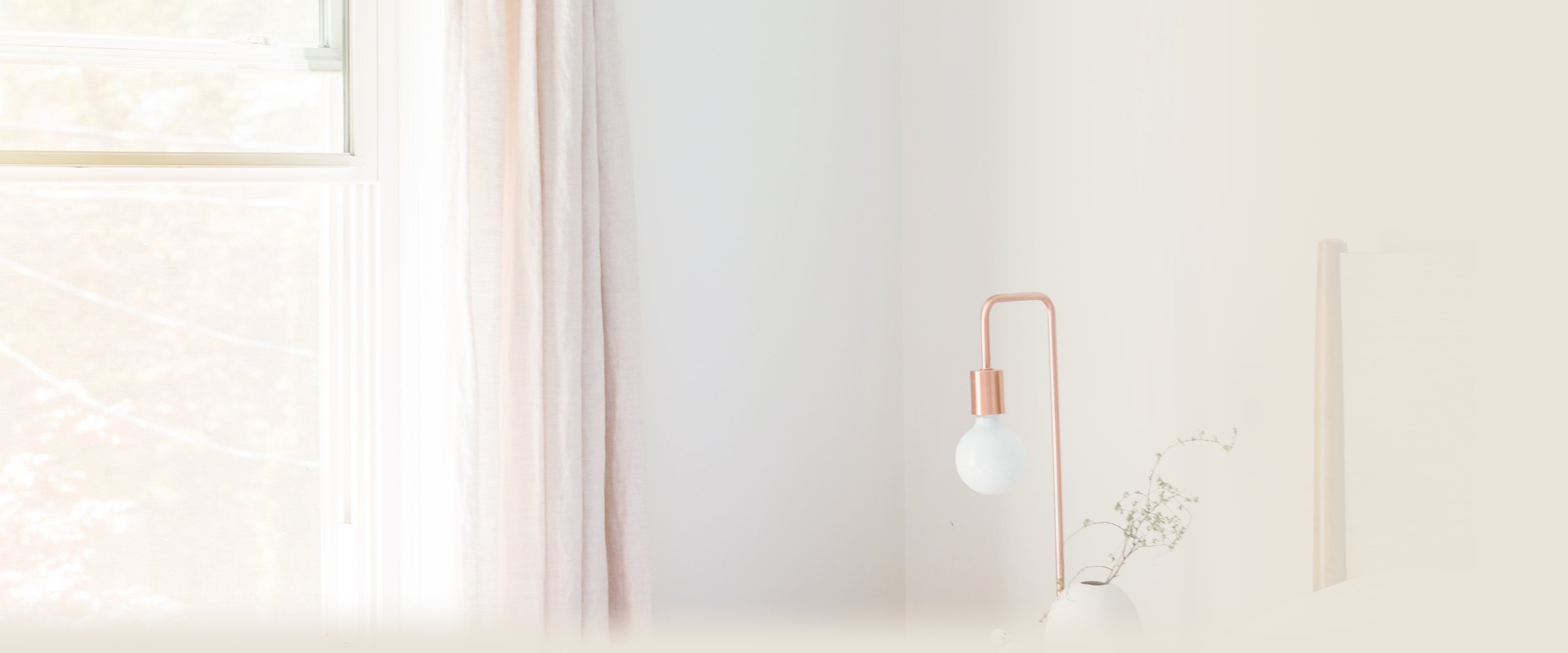 A freshly made bed beside a sunlit window in a simple, warm room.