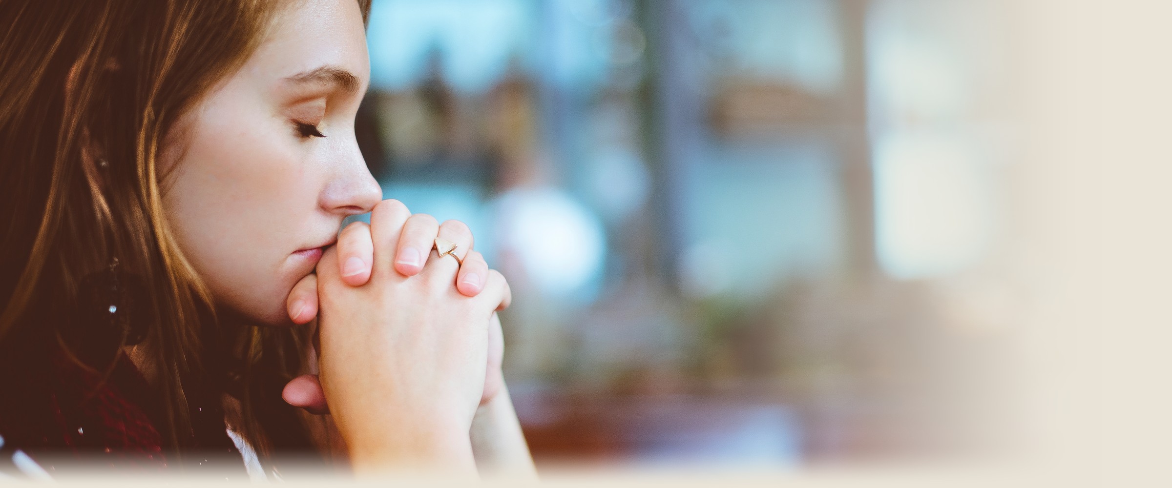 A young woman rests her clasped hands against her forehead in quiet prayer.